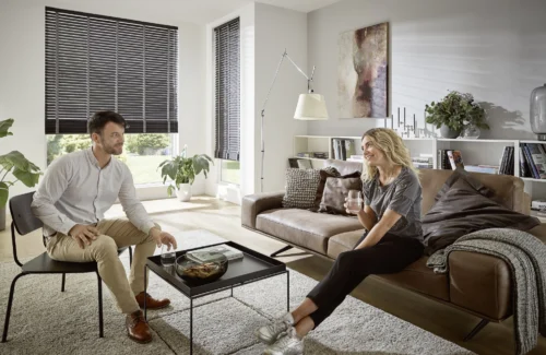 Paar unterhält sich im Wohnzimmer mit KADECO-Jalousien aus exklusivem Design-Filz