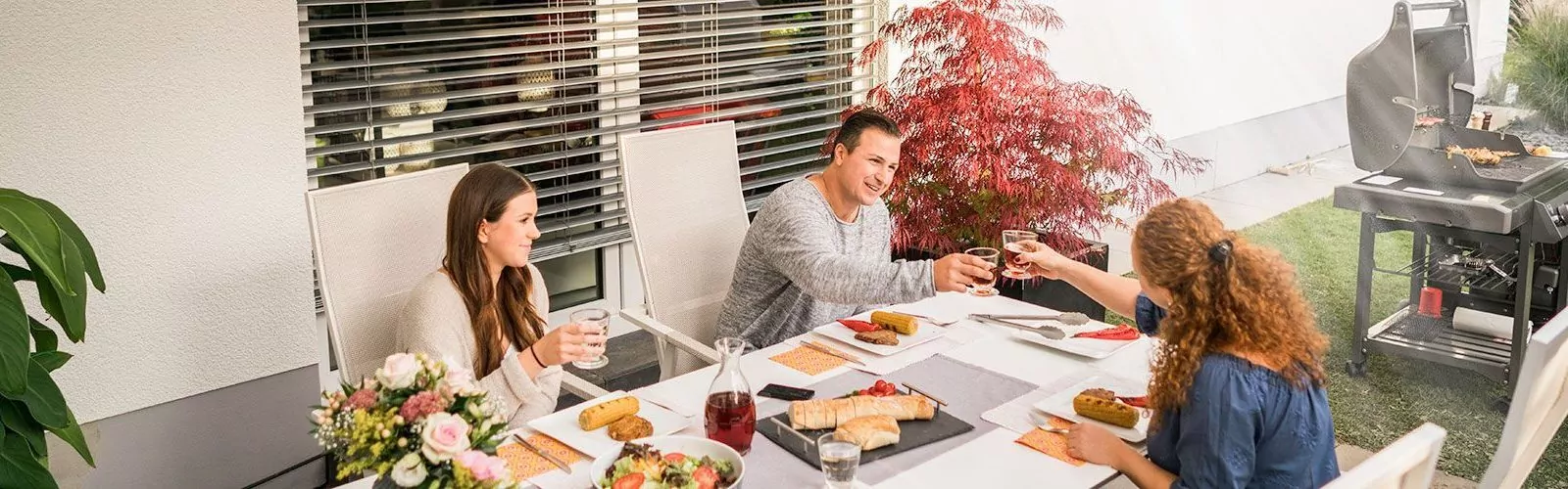 Familie sitzt auf der Terrasse und grillt